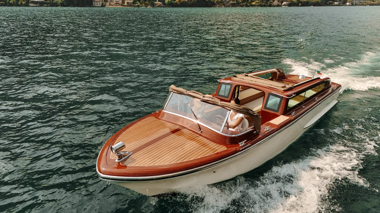 A wooden Venetian taxi boat under way on Lake Como, with the wooded shore behind it.