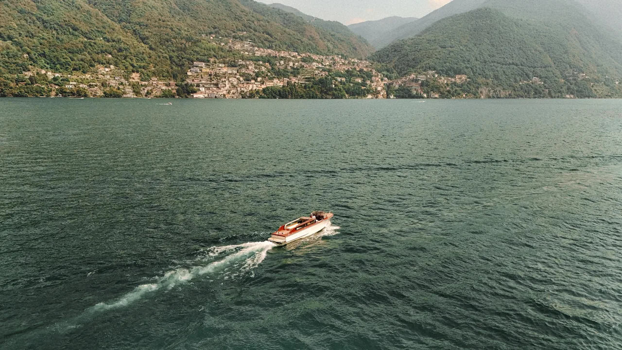 The boat crossing open water on Lake Como, with the villages of the shore behind.